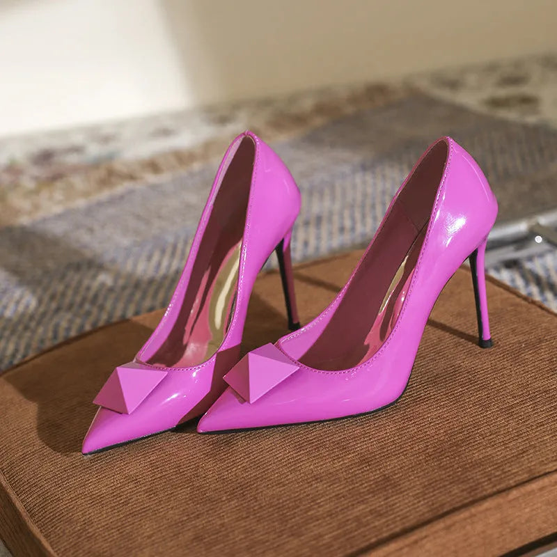 Pink patent leather women's pointed toe stiletto high heels with a rivet buckle.