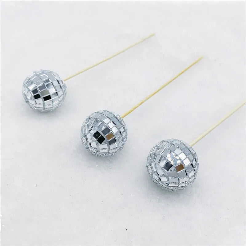 Glass mirror ball cake decoration on a wooden stick, showing reflective surface.