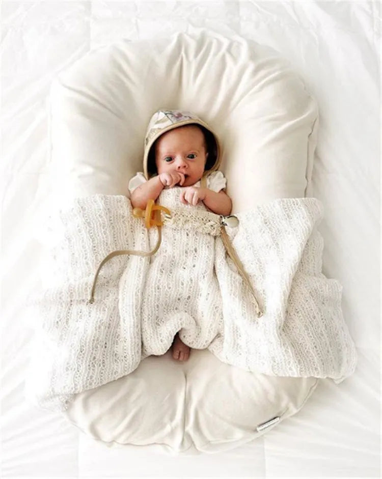 Beige portable baby nest crib cot for newborn infant on a bed
