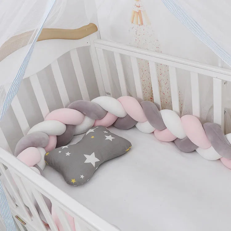 Braided knot style baby crib bumper in a light grey colour, shown lined inside a white wooden cot.