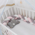 Braided knot style baby crib bumper in a light grey colour, shown lined inside a white wooden cot.