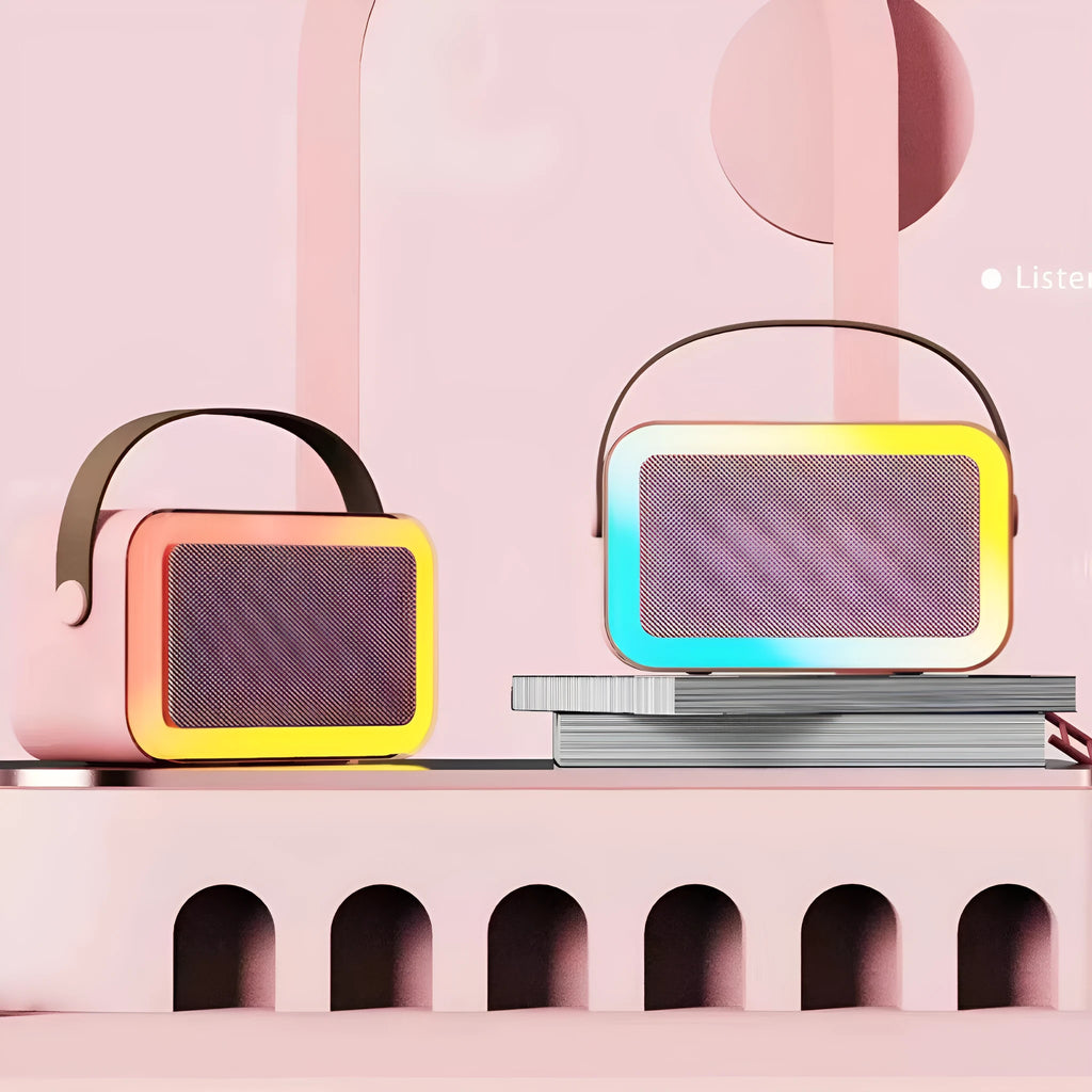 Pink portable Bluetooth karaoke speaker with microphone and coloured lights on a desk.