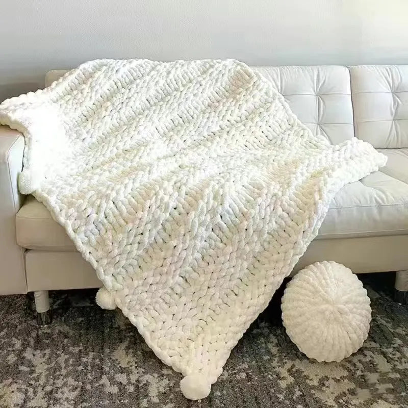 Coarse yarn chenille knitted blanket with braided gravity trim in a modern colour on a bed.
