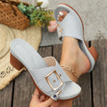 A pair of women's black retro-style slippers with a chunky heel and a prominent silver metal buckle across the instep.