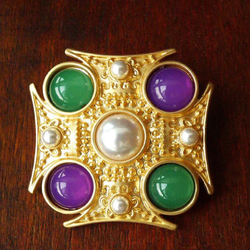 Close-up of a vintage baroque style zinc alloy brooch with a diamond shape on a dark fabric background.