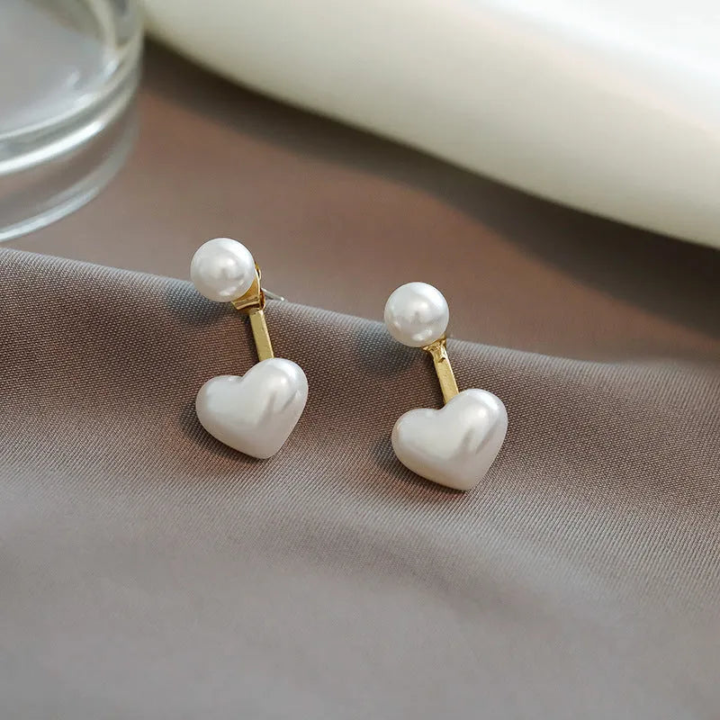 Close-up of simple heart-shaped alloy stud earrings with inlaid artificial gemstones.