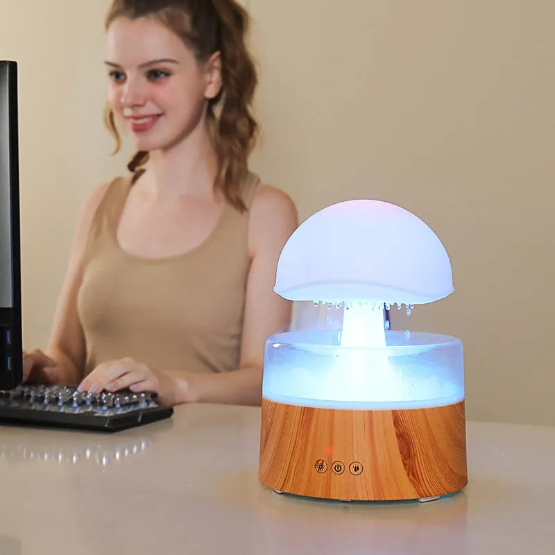 White cloud-shaped humidifier and aroma diffuser with LED lights and mist output on a wooden table.