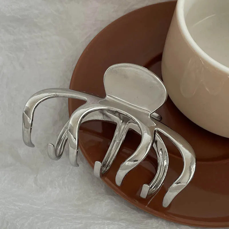 Assortment of silver metal hair claw barrettes with various designs including bows, pearls, and geometric shapes.