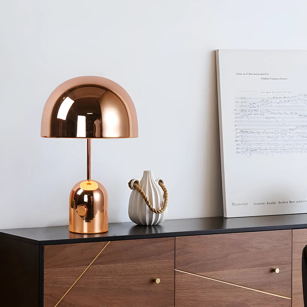 Mushroom-shaped table lamp with a metal base in rose gold finish on a wooden surface.