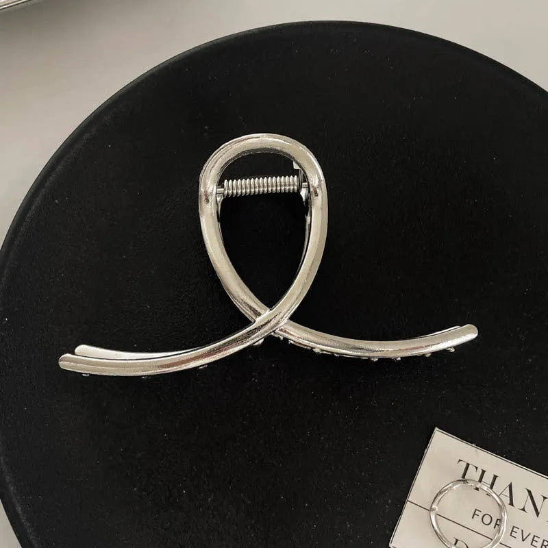 Assortment of silver metal hair claw barrettes with various designs including bows, pearls, and geometric shapes.