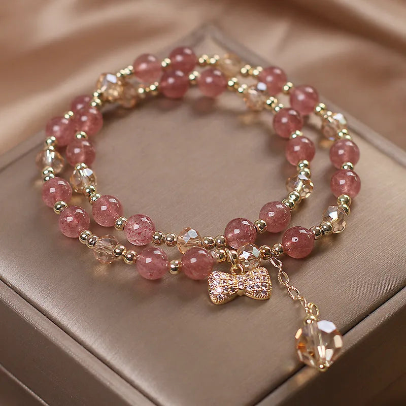 Women's double-layer strawberry quartz crystal bracelet with a red lucky cat charm on a white background.