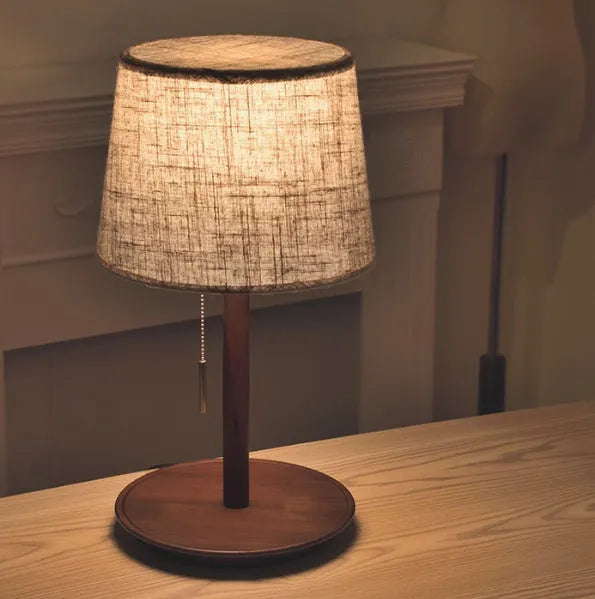 Walnut-colour solid wood desk lamp with a white fabric shade on a wooden table.