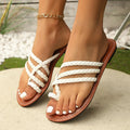 White women's clip-toe woven flat sandals with a rubber sole on a wooden floor.