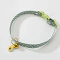 Adjustable green pet collar with a silver bell and a pink bow tie on a small dog.