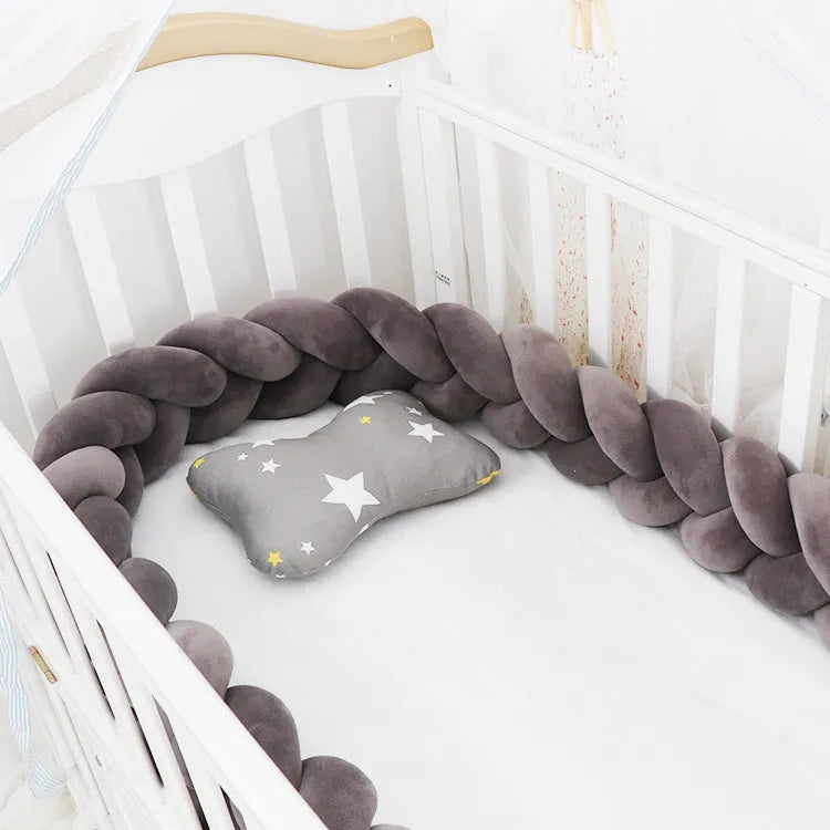 Braided knot style baby crib bumper in a light grey colour, shown lined inside a white wooden cot.