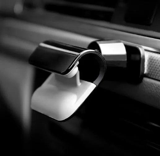 Black universal gravity car phone holder with 360-degree rotating head on a car dashboard.