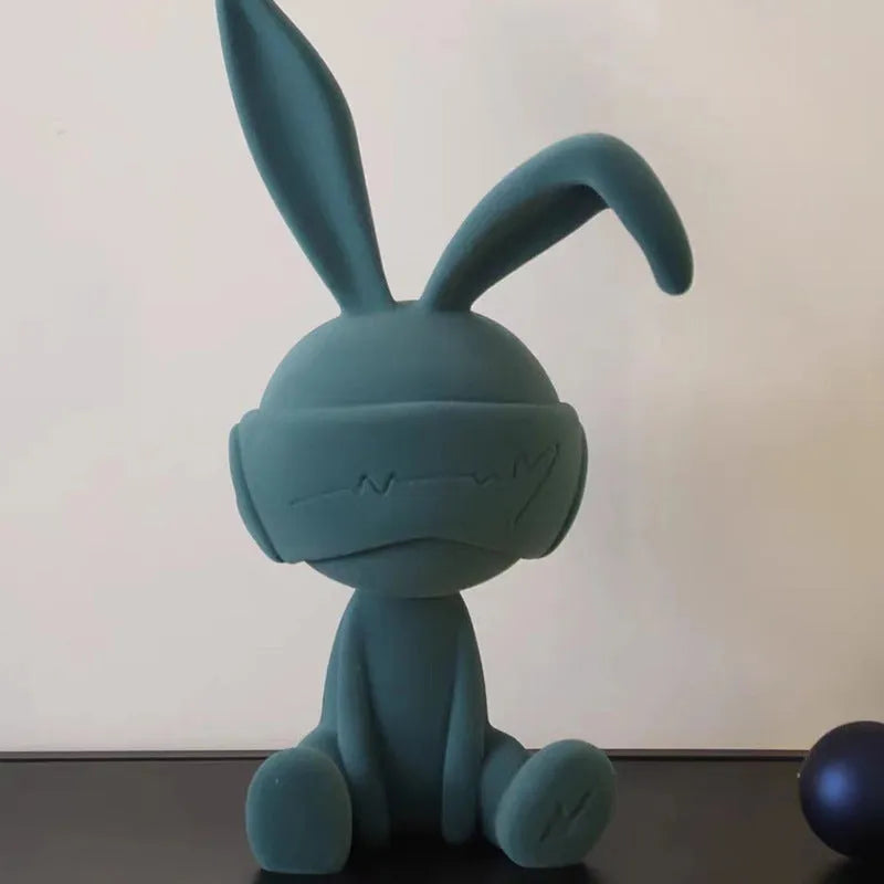 Suede blindfold rabbit resin table ornament in blue, green, or red colour on a shelf.
