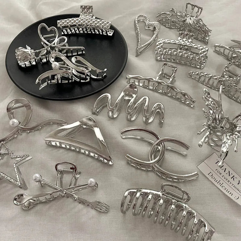 Assortment of silver metal hair claw barrettes with various designs including bows, pearls, and geometric shapes.