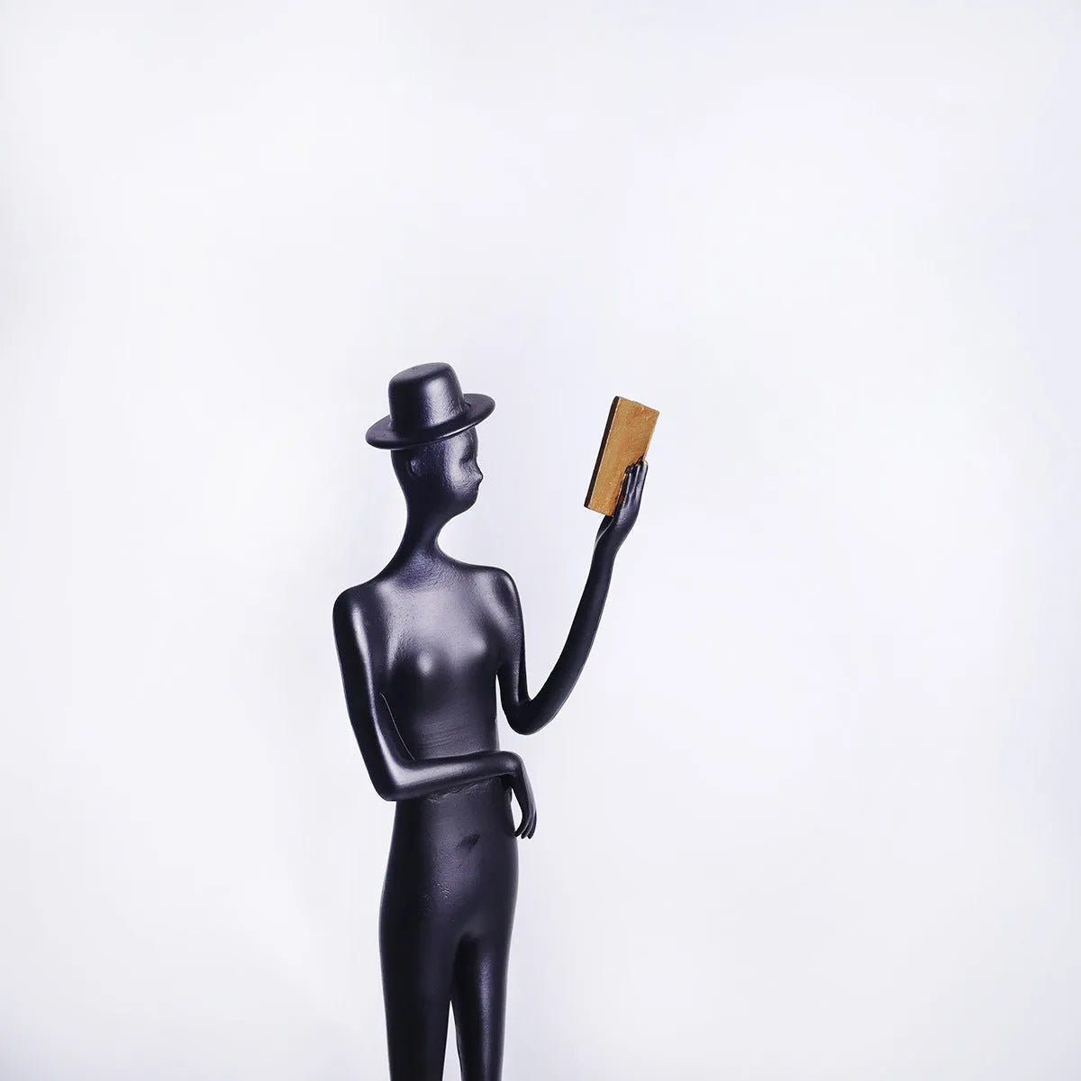Black cast aluminium reading woman sculpture on desktop, 12 cm wide by 51 cm high