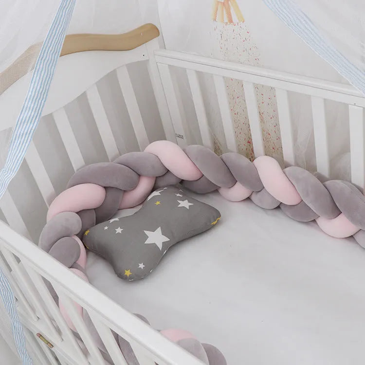 Braided knot style baby crib bumper in a light grey colour, shown lined inside a white wooden cot.