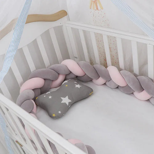 Braided knot style baby crib bumper in a light grey colour, shown lined inside a white wooden cot.