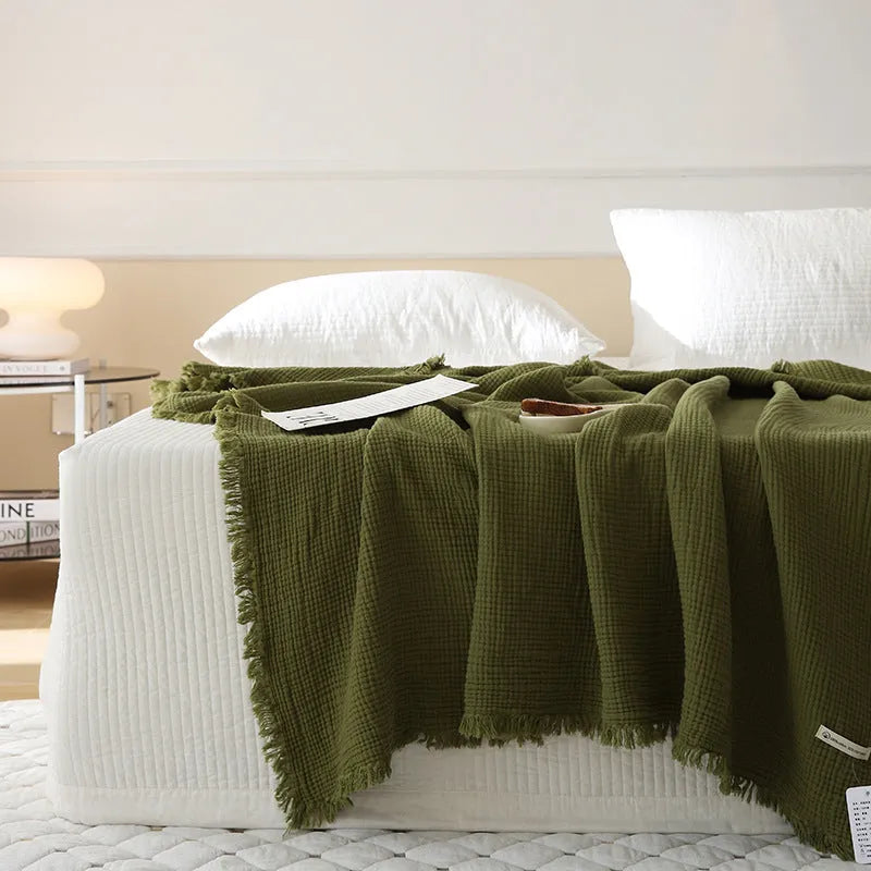 Four-layer gauze cotton blanket with tassel trim in avocado green colour draped over a sofa