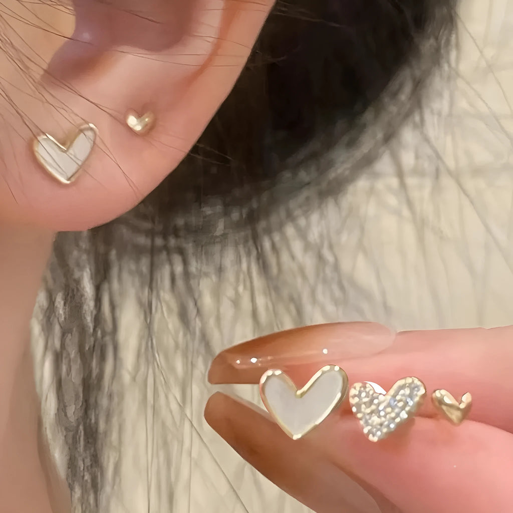 Three pairs of women's heart-shaped alloy earrings in gold, black, and pink colours on a white background.