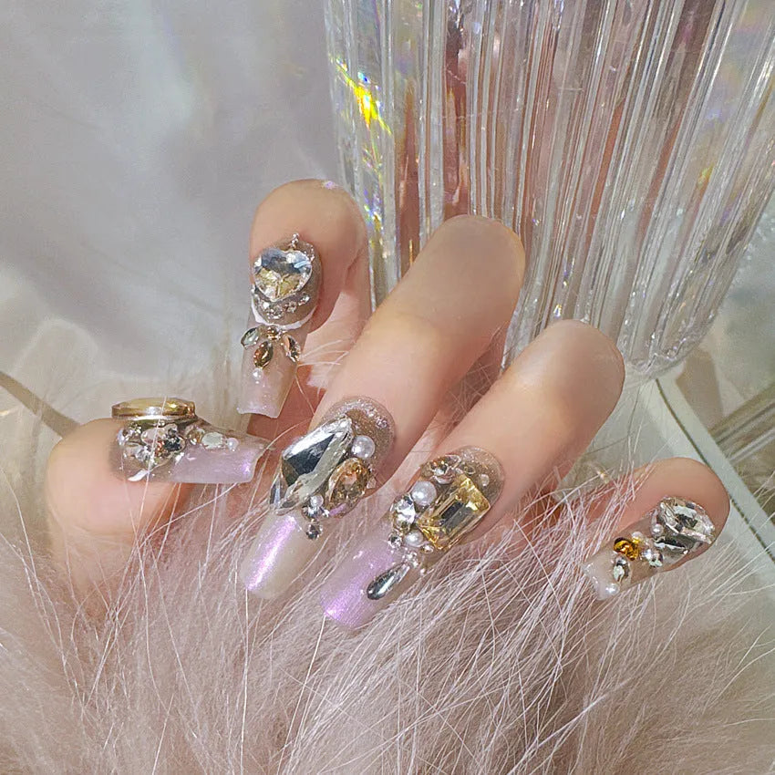 False nail patches with large rhinestones on card, shown with jelly adhesive pot and nail tools.