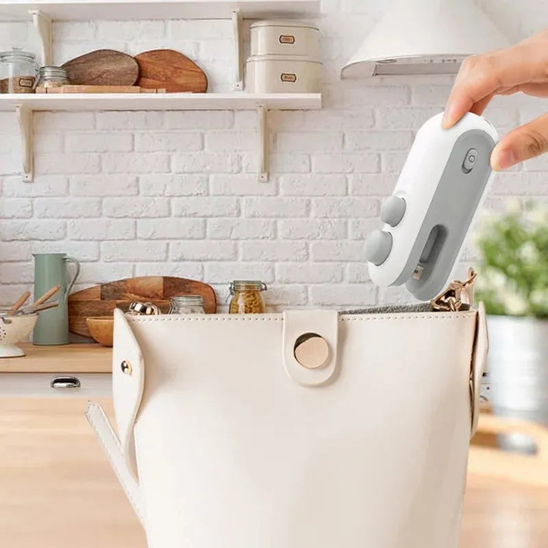 White and blue handheld USB rechargeable heat sealer with cutter blade.
