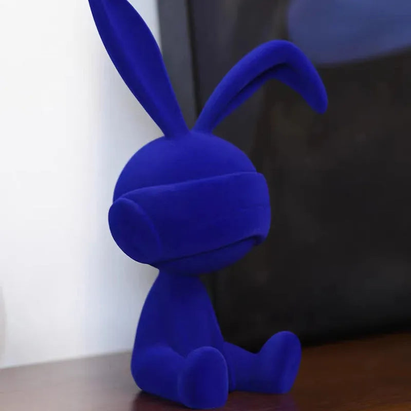 Suede blindfold rabbit resin table ornament in blue, green, or red colour on a shelf.