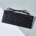 Compact black wired USB keyboard with noiseless keys next to notebook computer