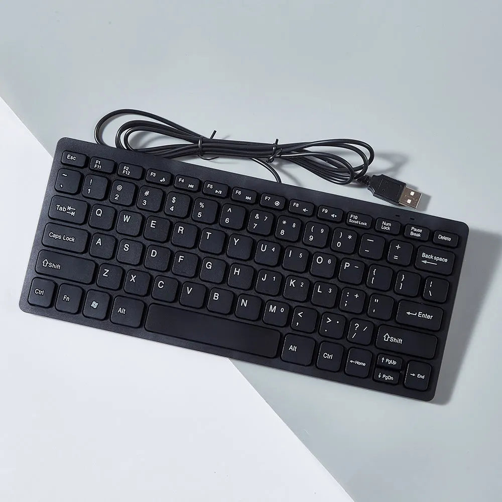 Compact black wired USB keyboard with noiseless keys next to notebook computer