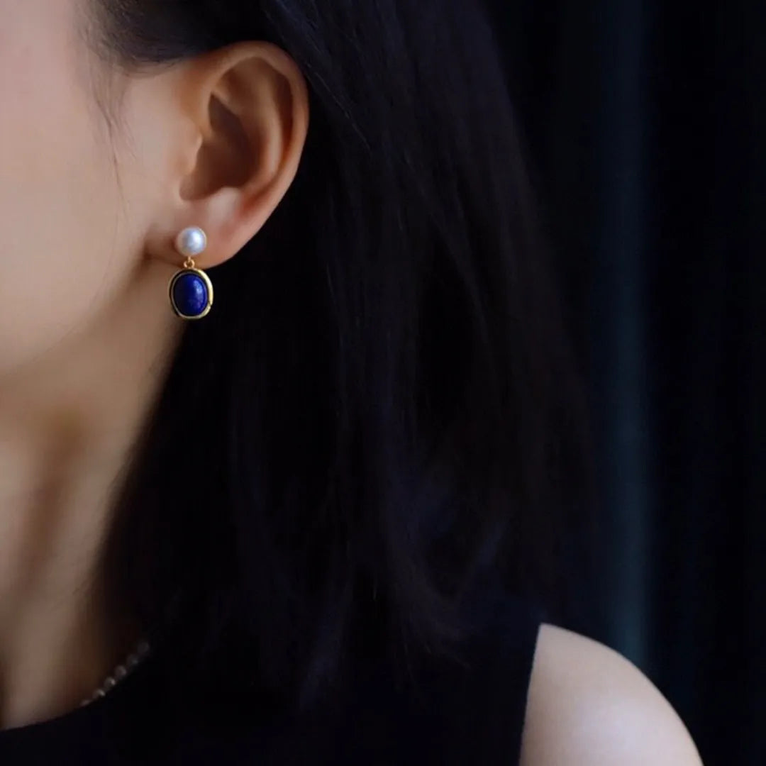 A pair of simple stud earrings with a blue lapis lazuli pearl set in a sterling silver setting.