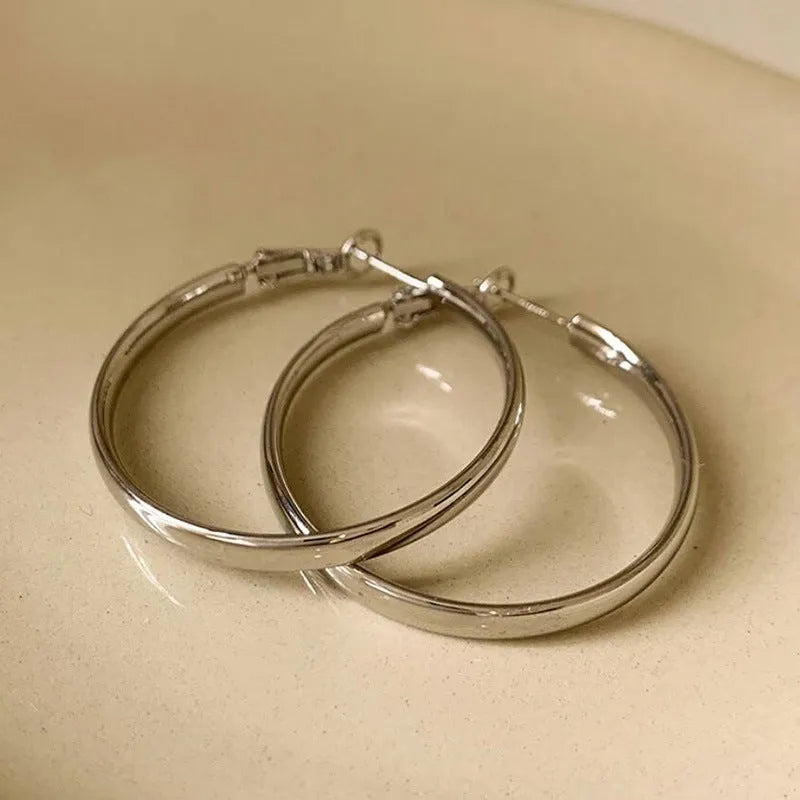 A pair of 40mm circular metal earrings in a gold or silver electroplated finish on a copper base