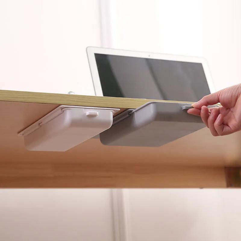 White plastic adhesive under desk storage drawer box with a lid and internal divider grid for organisation.