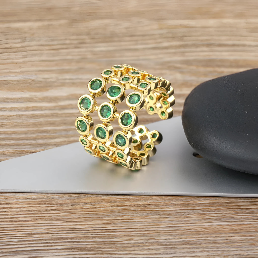 Copper ring with 18K gold plating and large green zirconia stones in an exaggerated wide-band design.