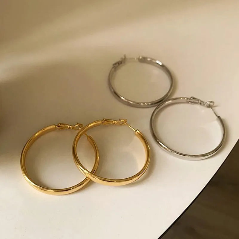 A pair of 40mm circular metal earrings in a gold or silver electroplated finish on a copper base