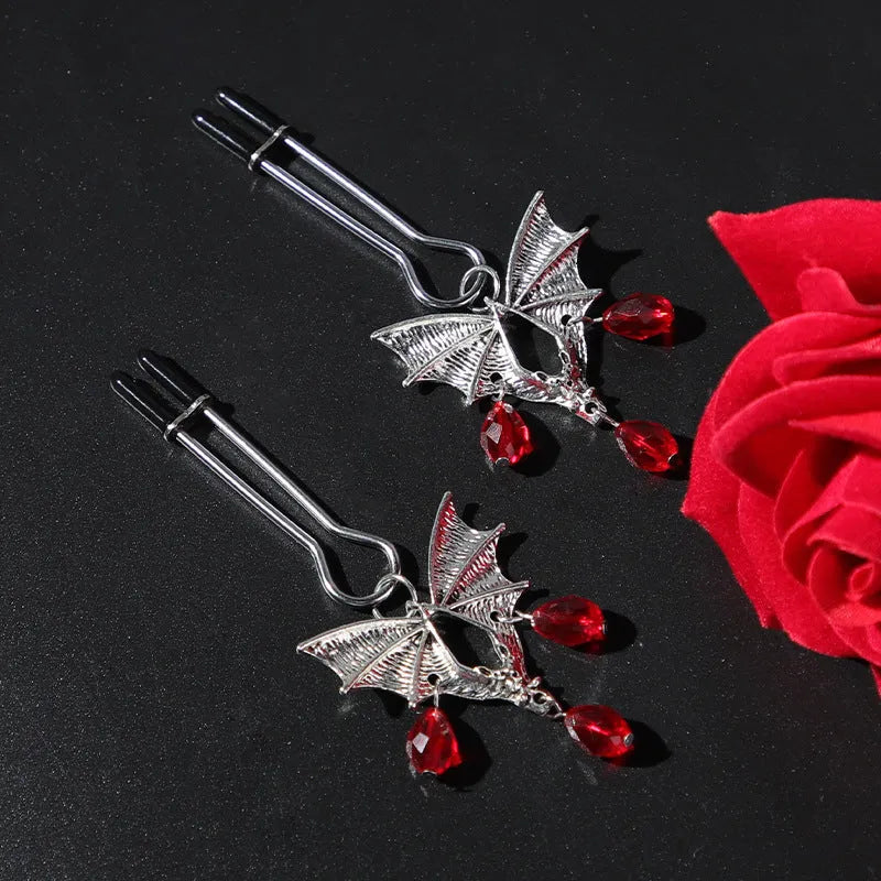 Silver bat-shaped adjustable nipple clamps with ruby decoration on a black background