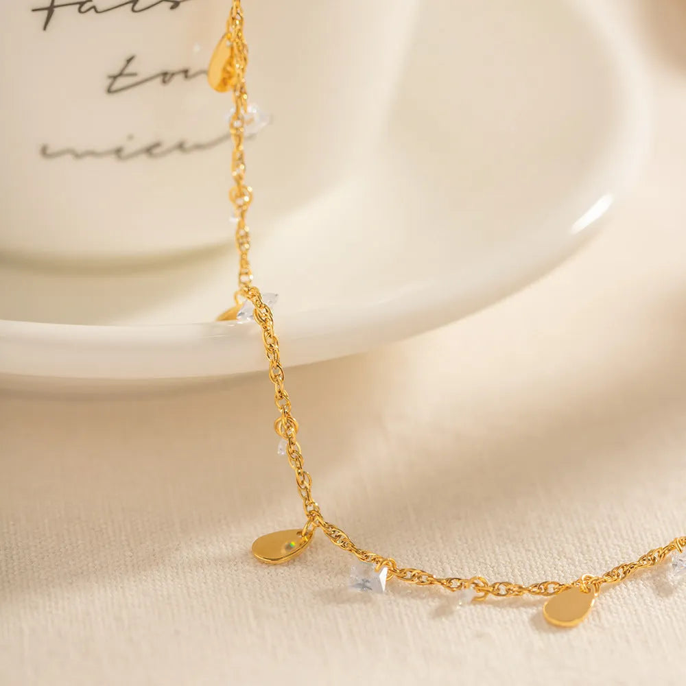 Close-up of a stainless steel geometric anklet with a personalised water drop tassel pendant.