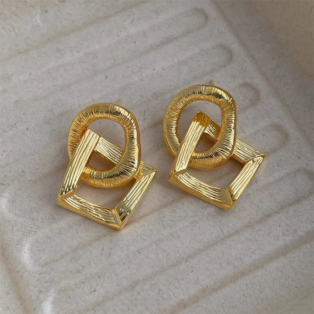 Geometric retro-style drop earrings with a circular pendant, available in gold and silver.