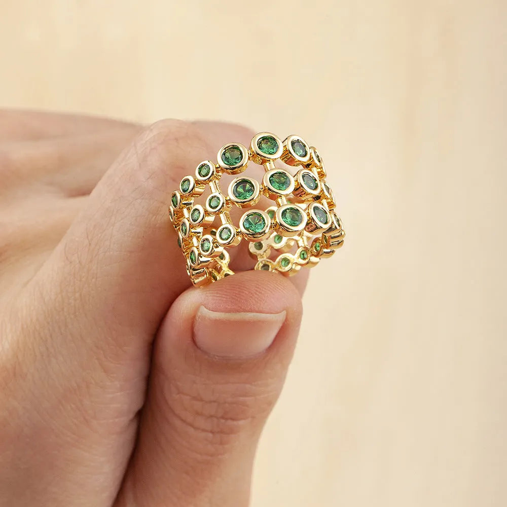 Copper ring with 18K gold plating and large green zirconia stones in an exaggerated wide-band design.