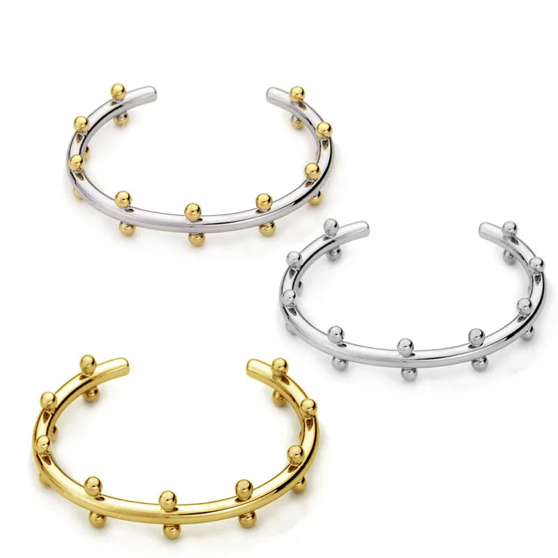 Stainless steel bracelet with C-shaped bean bead charm featuring texture and rivet details.