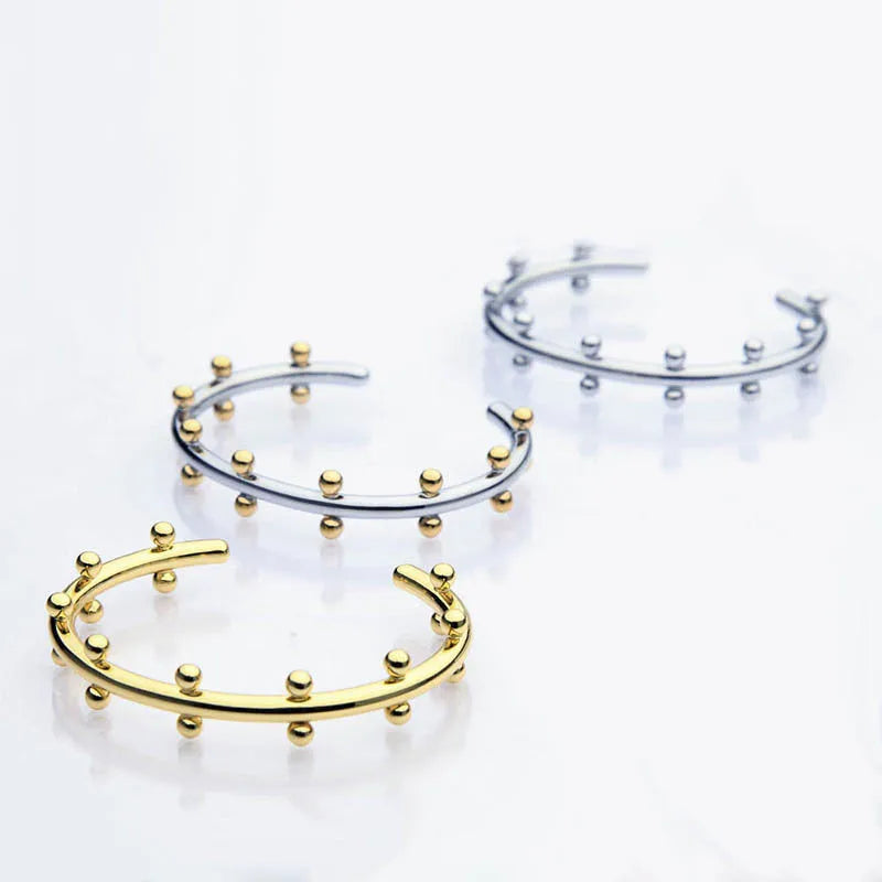 Stainless steel bracelet with C-shaped bean bead charm featuring texture and rivet details.