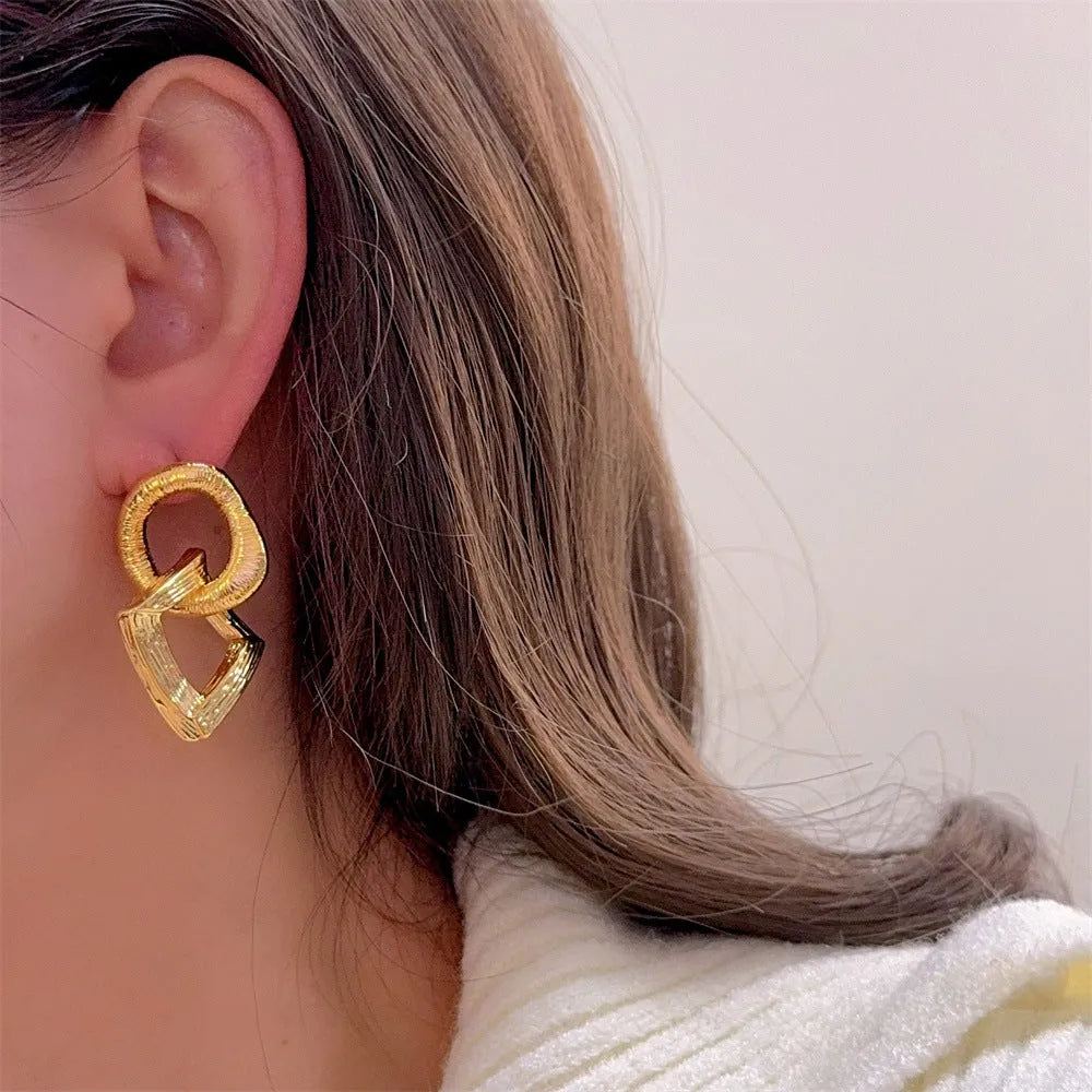 Geometric retro-style drop earrings with a circular pendant, available in gold and silver.
