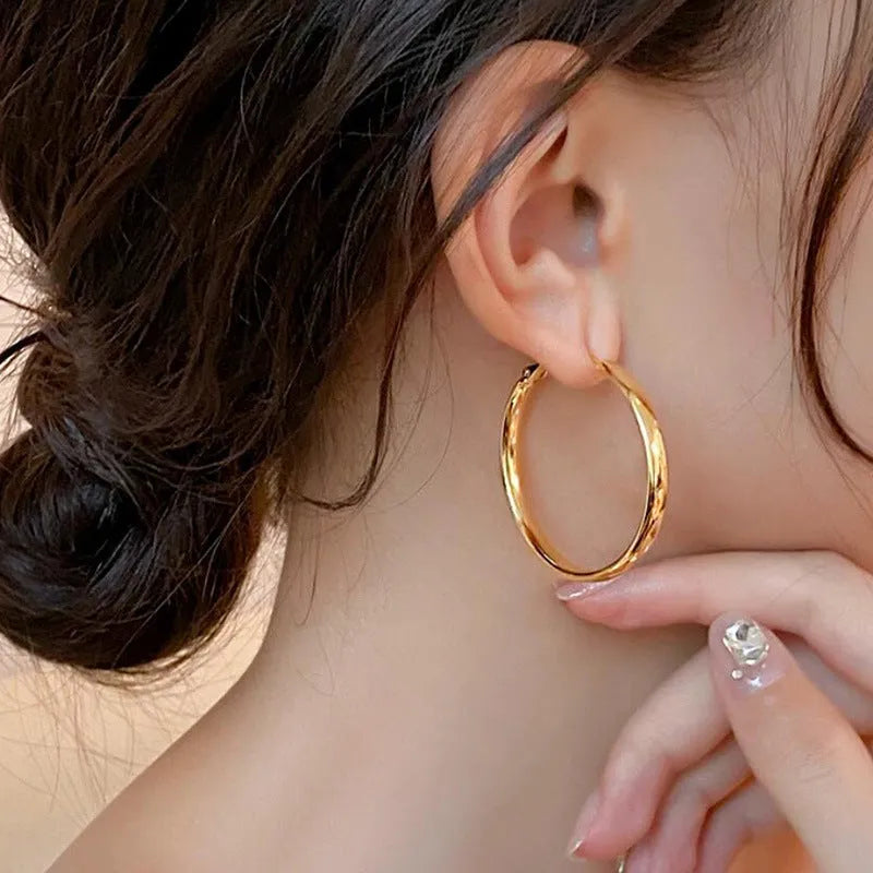 A pair of 40mm circular metal earrings in a gold or silver electroplated finish on a copper base