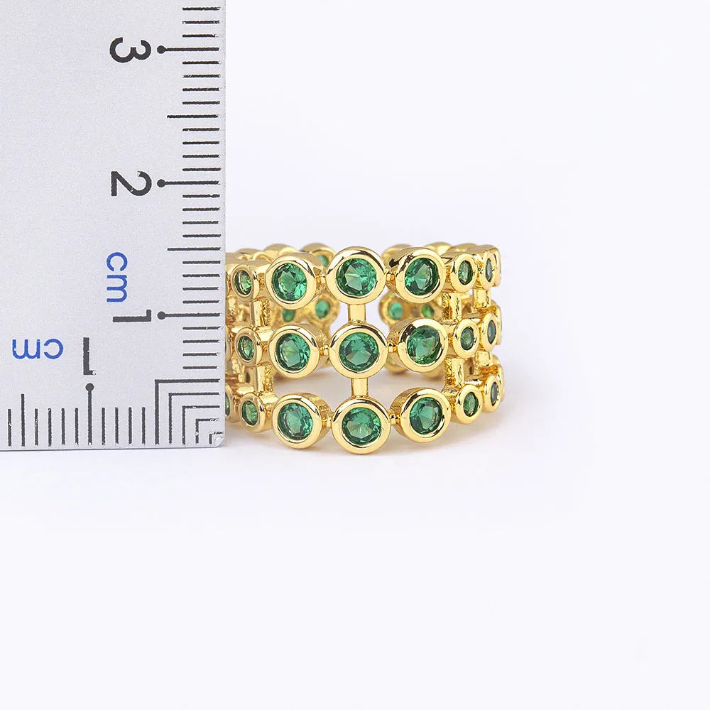 Copper ring with 18K gold plating and large green zirconia stones in an exaggerated wide-band design.