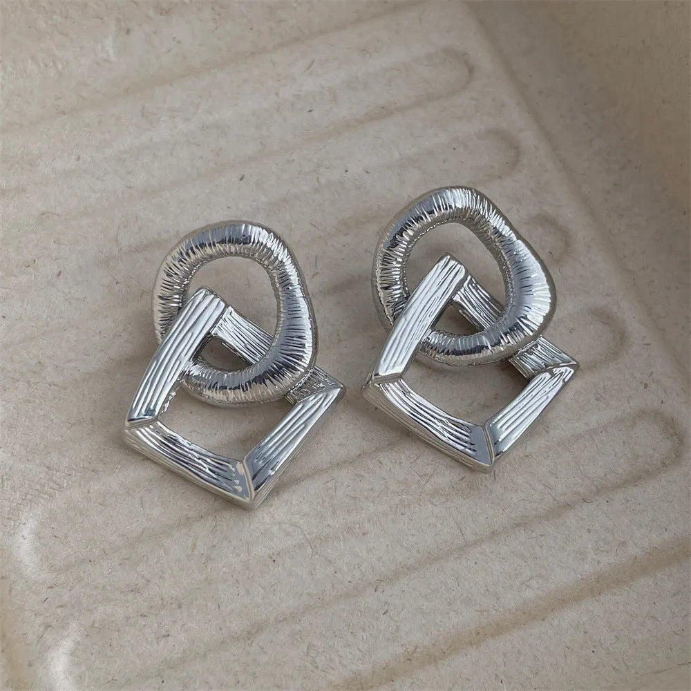 Geometric retro-style drop earrings with a circular pendant, available in gold and silver.