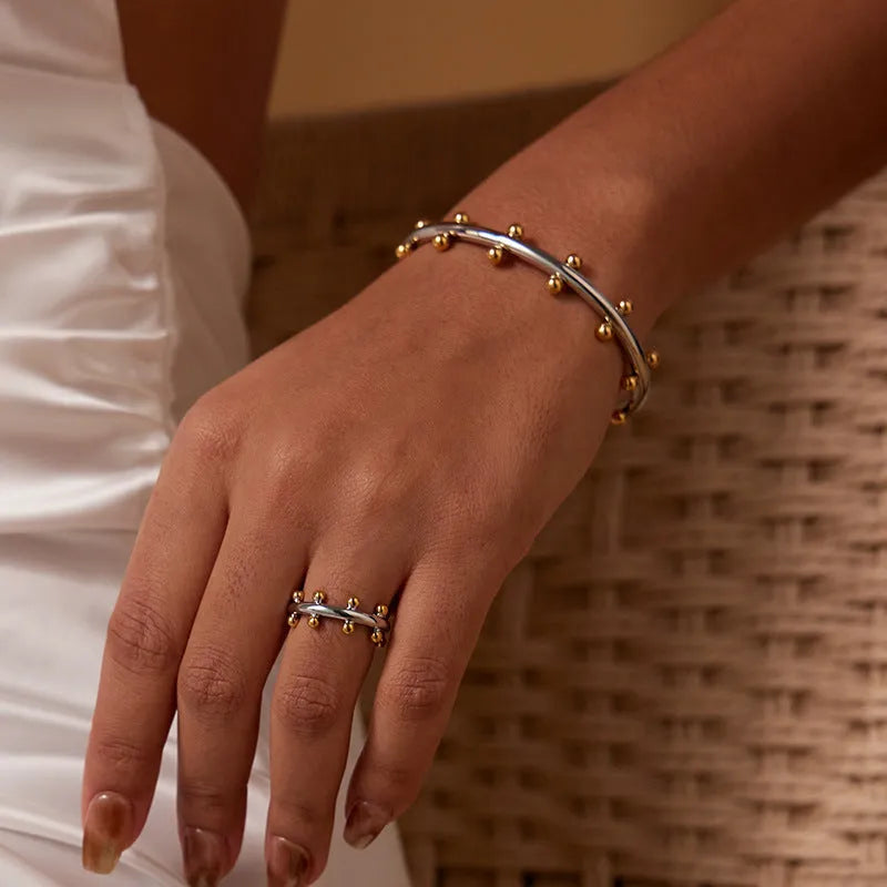 Stainless steel bracelet with C-shaped bean bead charm featuring texture and rivet details.