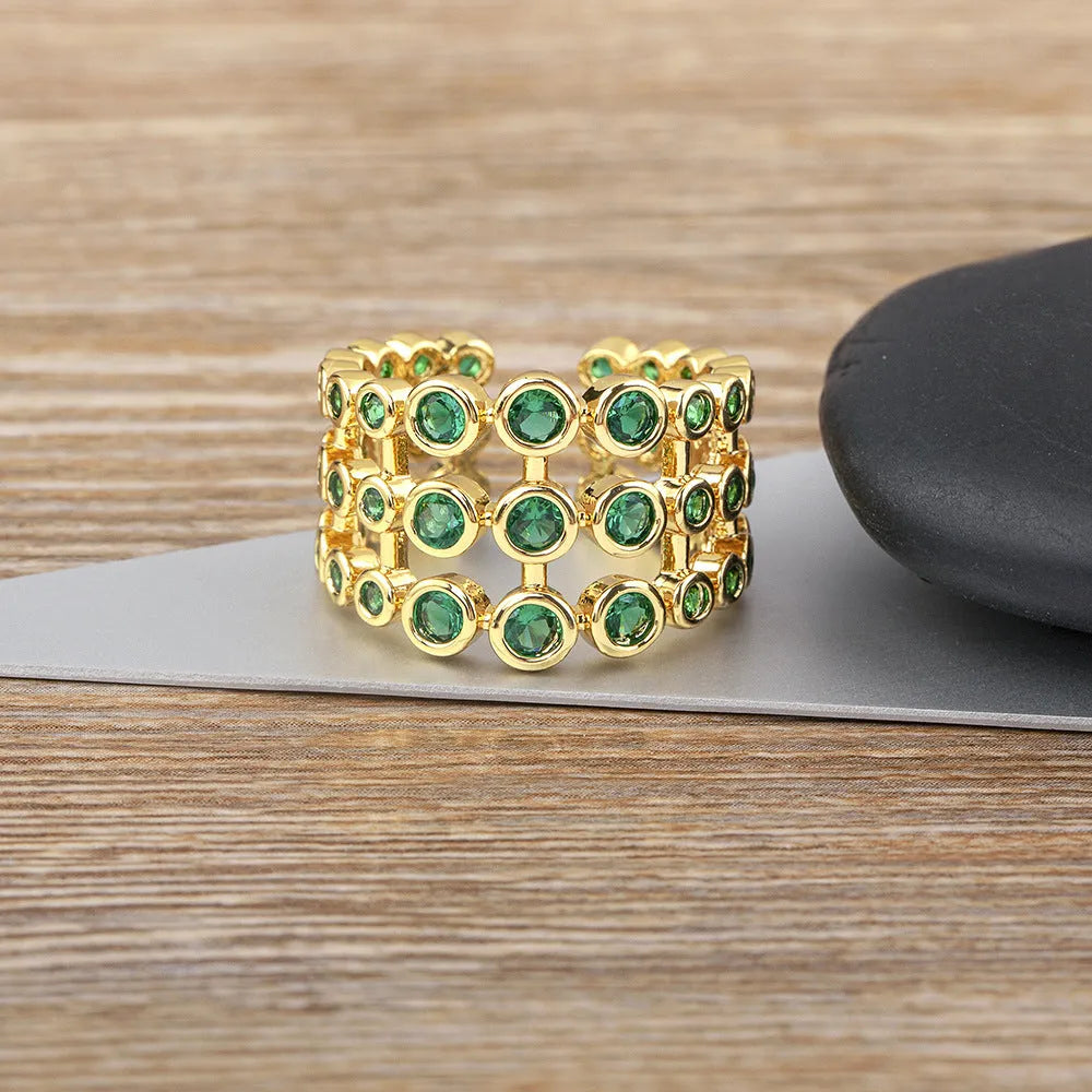 Copper ring with 18K gold plating and large green zirconia stones in an exaggerated wide-band design.