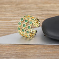 Copper ring with 18K gold plating and large green zirconia stones in an exaggerated wide-band design.